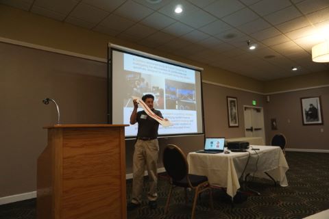 Man standing in front of a projector holds up sample retroreflective pavement marker with red arrow.