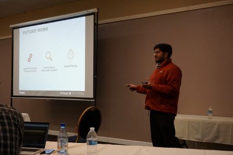 A man gestures while speaking next to a projector screen showing a slide about future work.