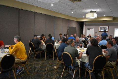 People eat dinner and talk to one another around several tables.