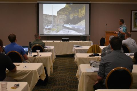 A man presents in front of an audience. The projector displays a photo of a road intersection.