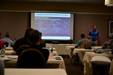 A man presents in front of a projector screen.