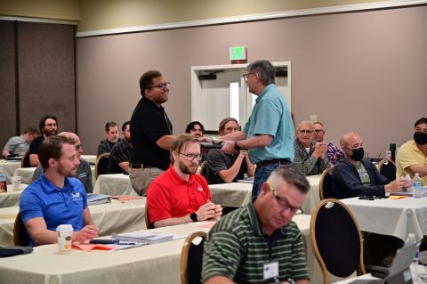 Two men stand in the audience. One hands the other a certificate.
