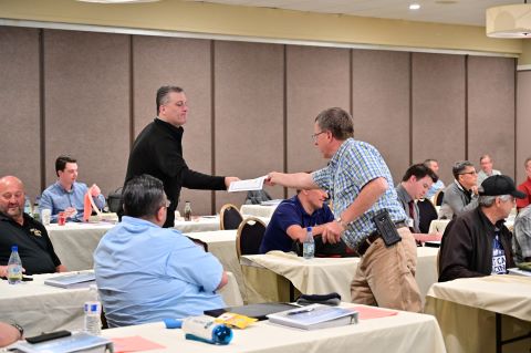 Two men stand in the audience. One hands the other a certificate.