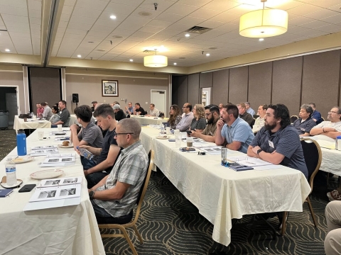An audience seated at tables looks towards the front of a room.