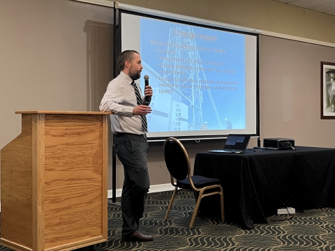 A man with a microphone presents in front of an audience.