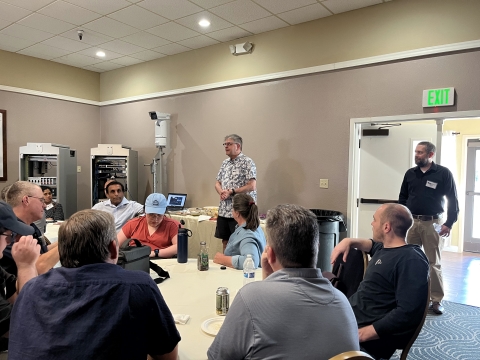A man speaks to an audience that is seated at round tables.