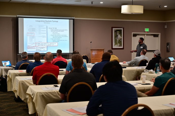 An audience watches a man present beside a projector.