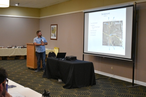 While presenting, a man points to the screen with a slide showing a map.