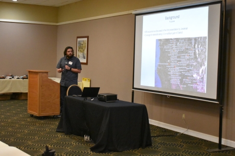 A man presents beside a projector screen.