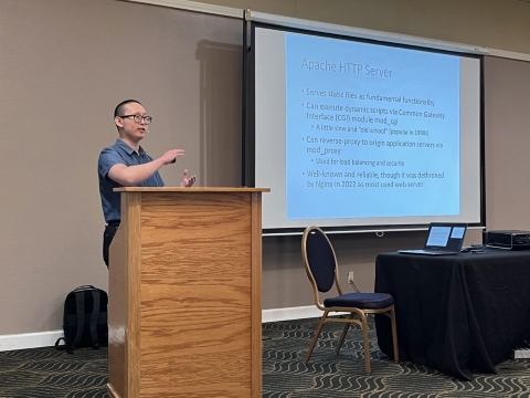 A man presents from behind a podium. A slide on a screen lists bullet points under Apache HTTP Server.